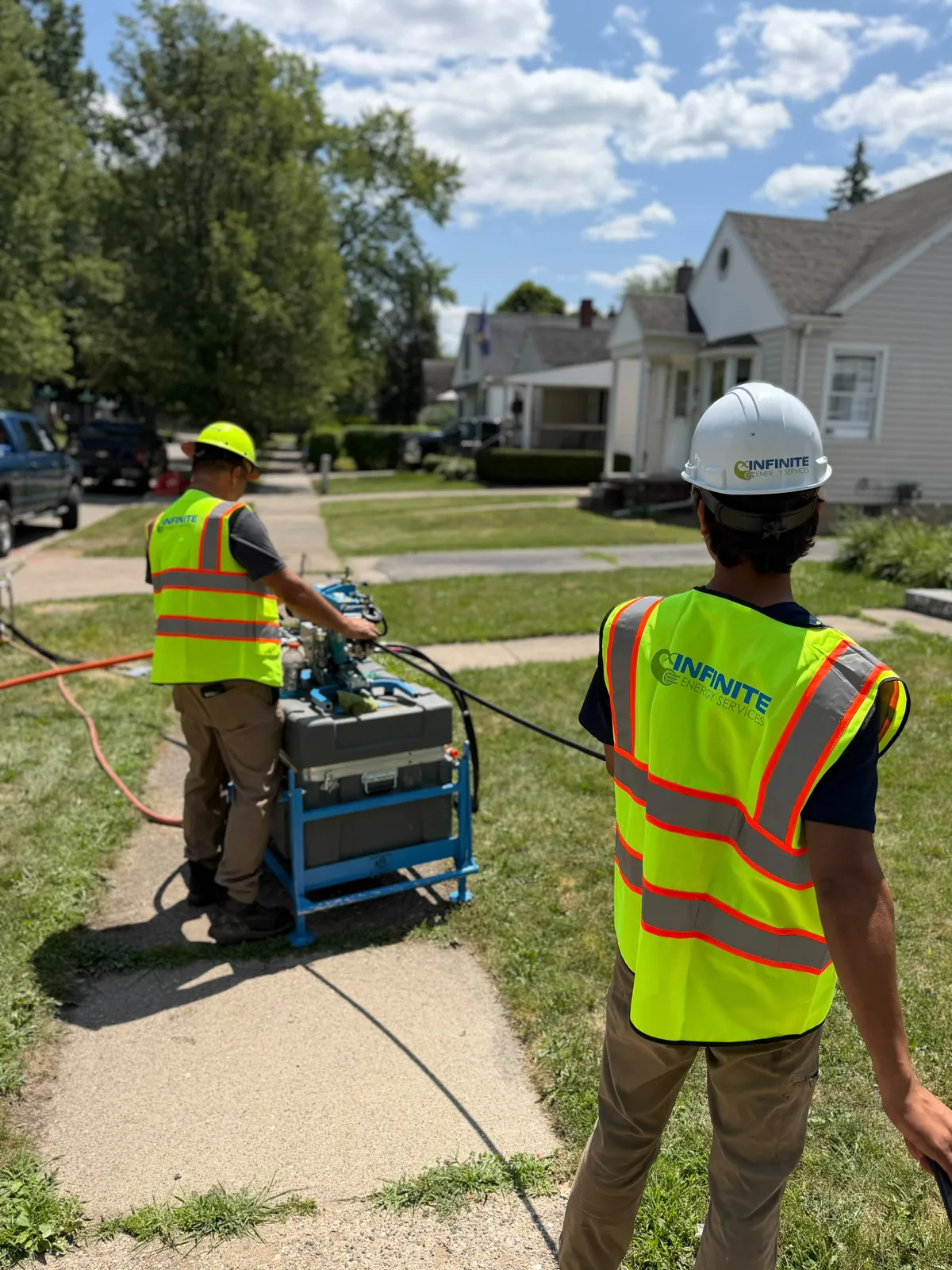 Two Infinite Energy Services crew members running a fiber blowing machine on a residential street
